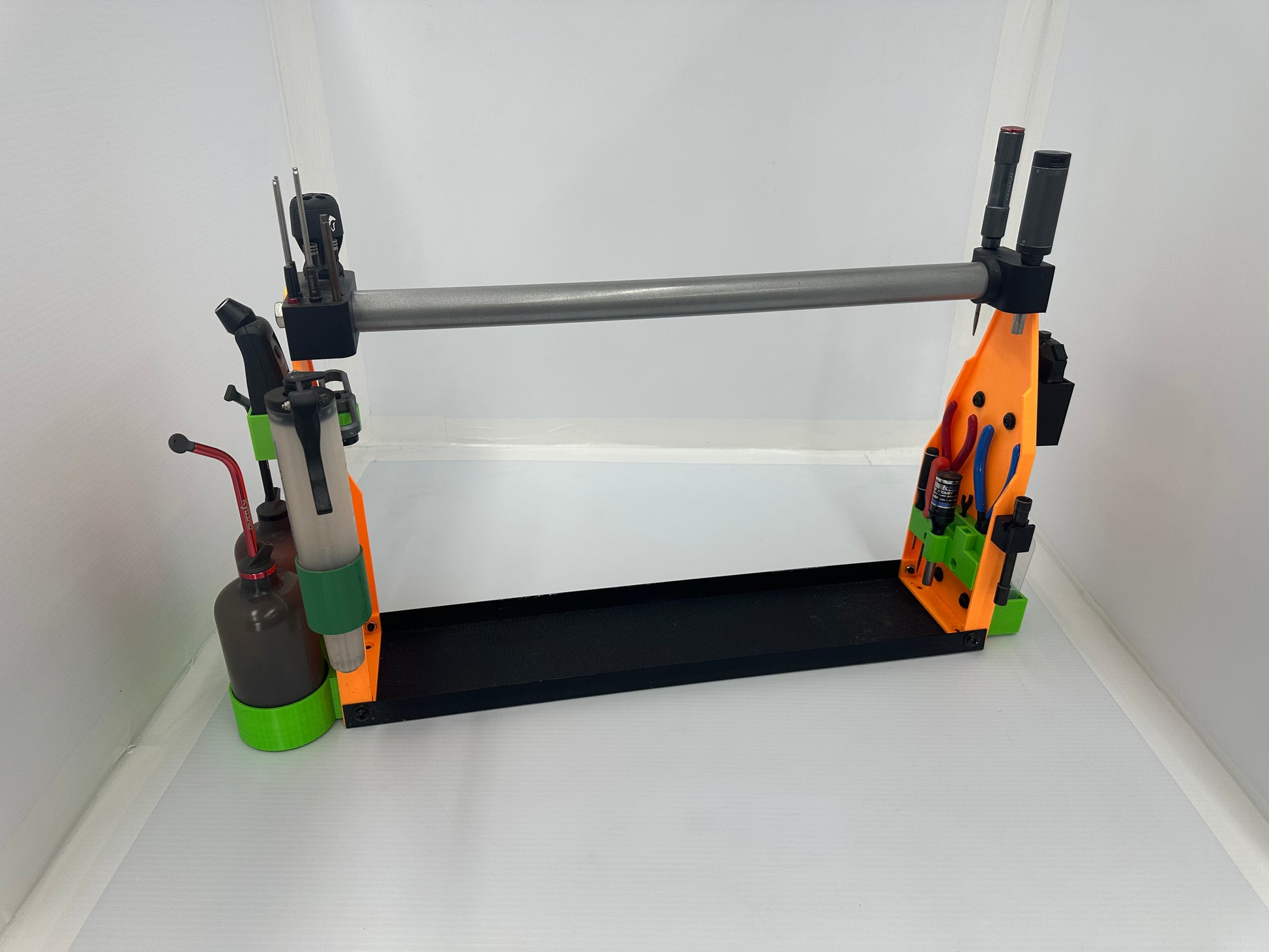 A 3D-printed DIY tool holder and workbench organizer, featuring a black base, orange and green side brackets, a silver metal bar, and various small hand tools, shown on a white background.